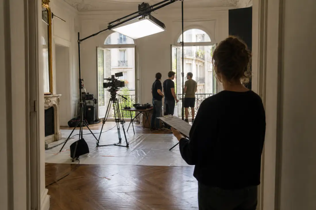 Équipe de tournage installant caméra, éclairages et protections de sol dans le salon d’un appartement ancien.
