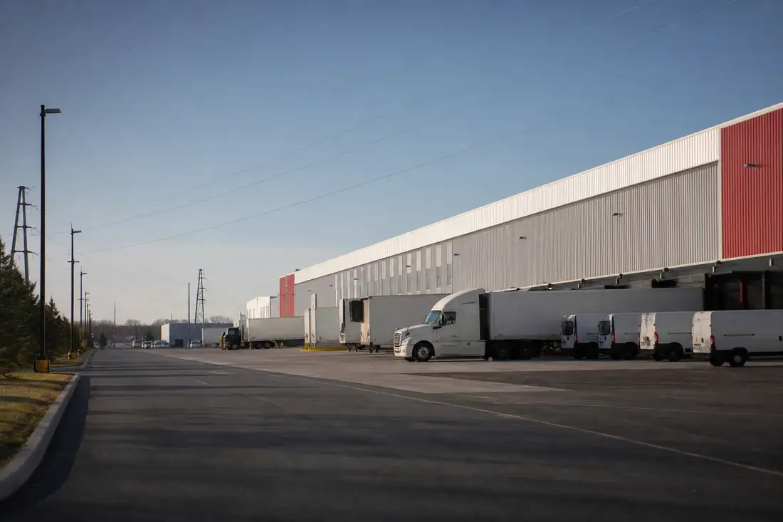 Entrepôt logistique américain avec quais de chargement, camions et voies d’accès dans une zone industrielle.