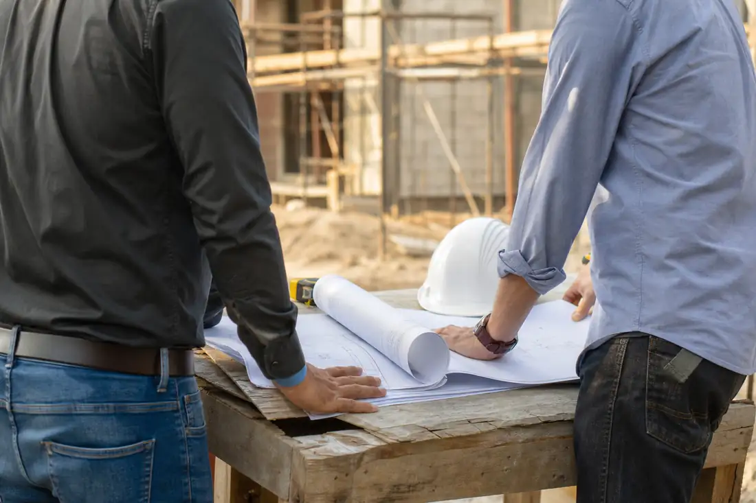 Architecte et chef de chantier consultant des plans de construction devant une maison en cours d’édification