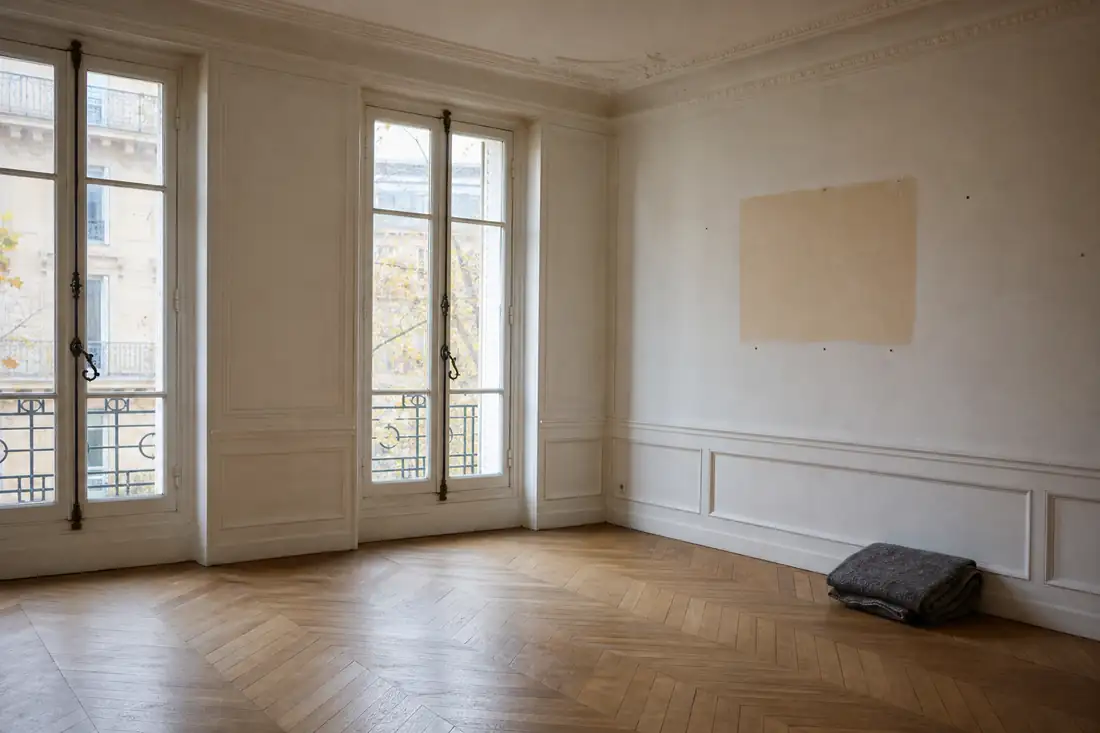 Appartement vide au parquet nu et aux moulures anciennes, en attente de vente dans la lumière grise d’une cour
