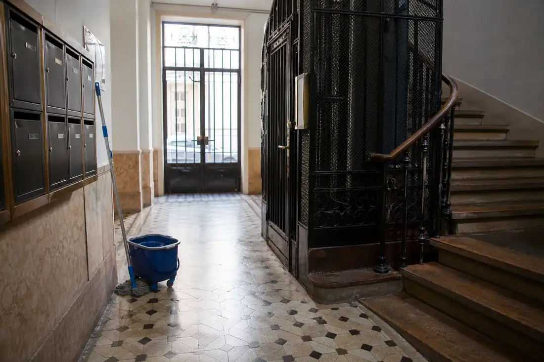 Hall d’immeuble collectif avec boîtes aux lettres, cage d’ascenseur ancienne et sol carrelé fraîchement entretenu