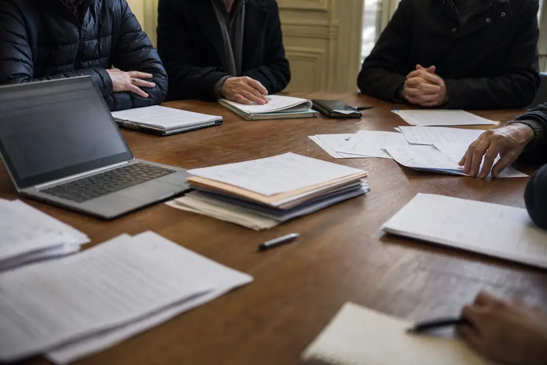 Réunion tendue de copropriétaires autour de documents de gestion dans le hall d'un immeuble