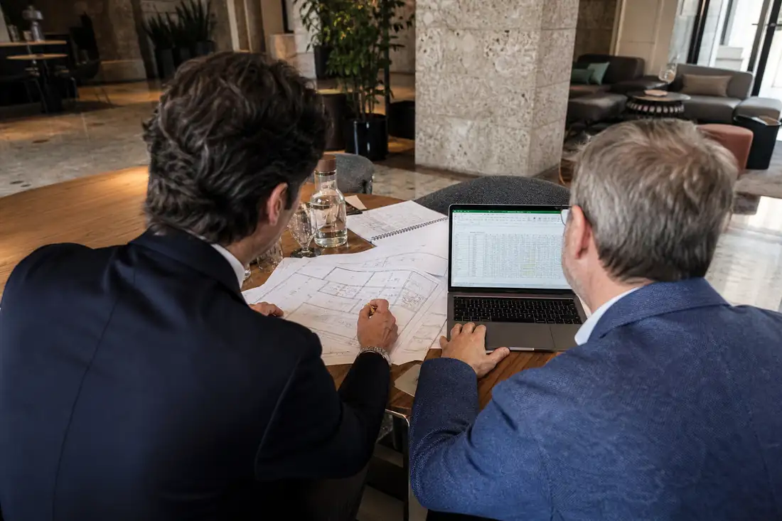 Conseillers examinant des plans dans le hall d’un hôtel d’affaires italien, vus de dos sans visage identifiable.