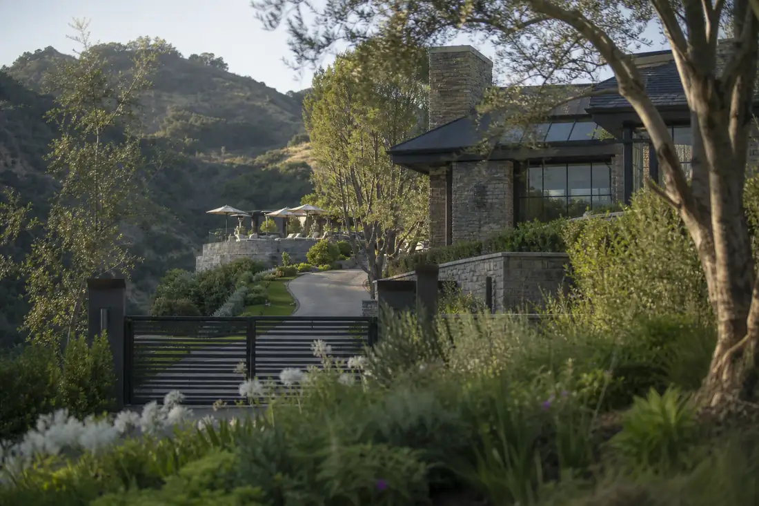 Demeure contemporaine haut de gamme entourée d’arbres, avec façade vitrée et terrasse discrète en hauteur.
