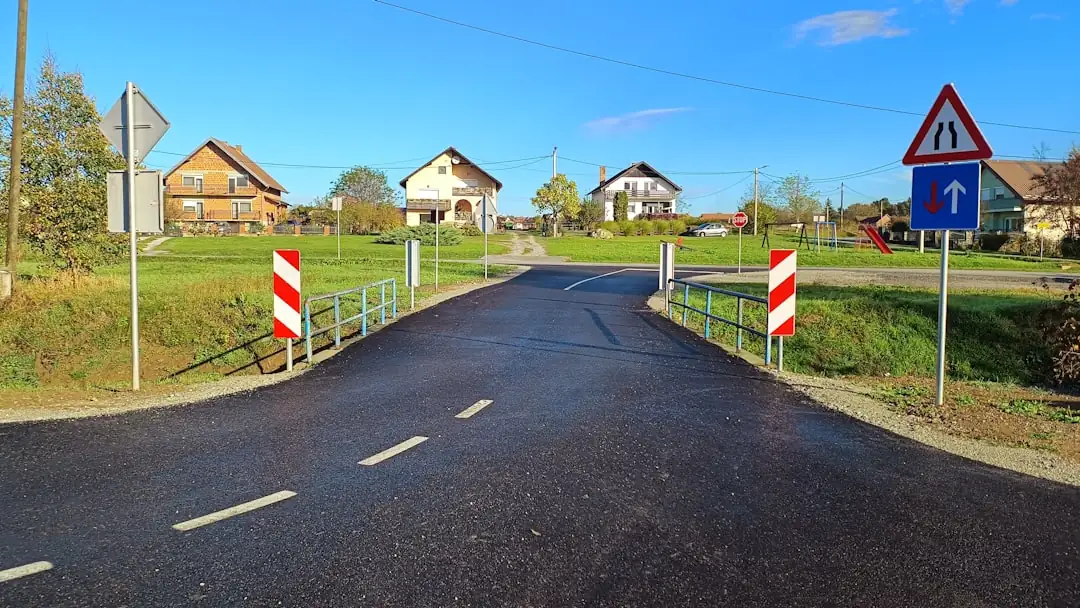 Ensemble de commerces en bord de route avec parking, accès véhicules et enseignes volontairement illisibles.