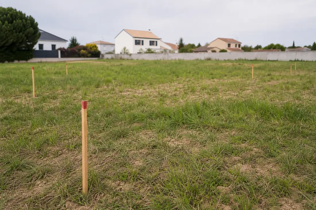 Terrain vide borné par des piquets d’arpentage à l’intérieur d’un lotissement résidentiel