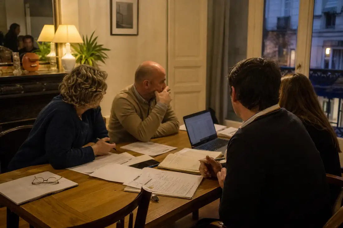 Réunion de copropriétaires autour d’un dossier de gestion dans le hall d’un petit immeuble