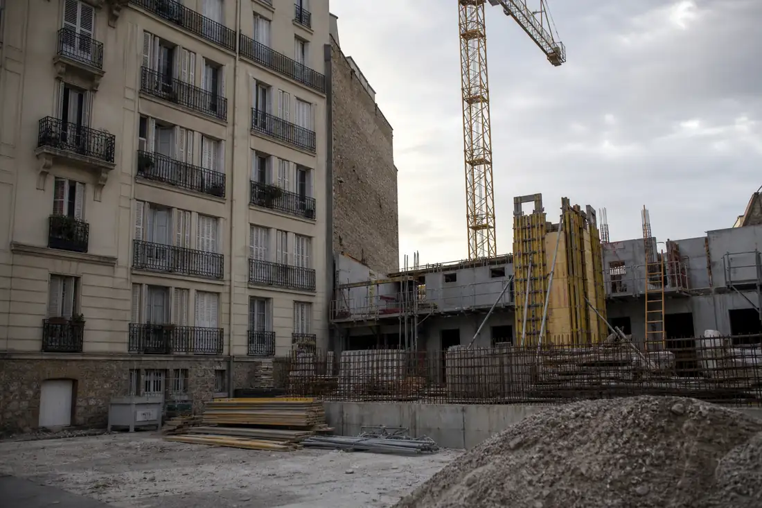 Chantier de construction adossé à un immeuble d’habitation, échafaudages et grue vus depuis les balcons voisins