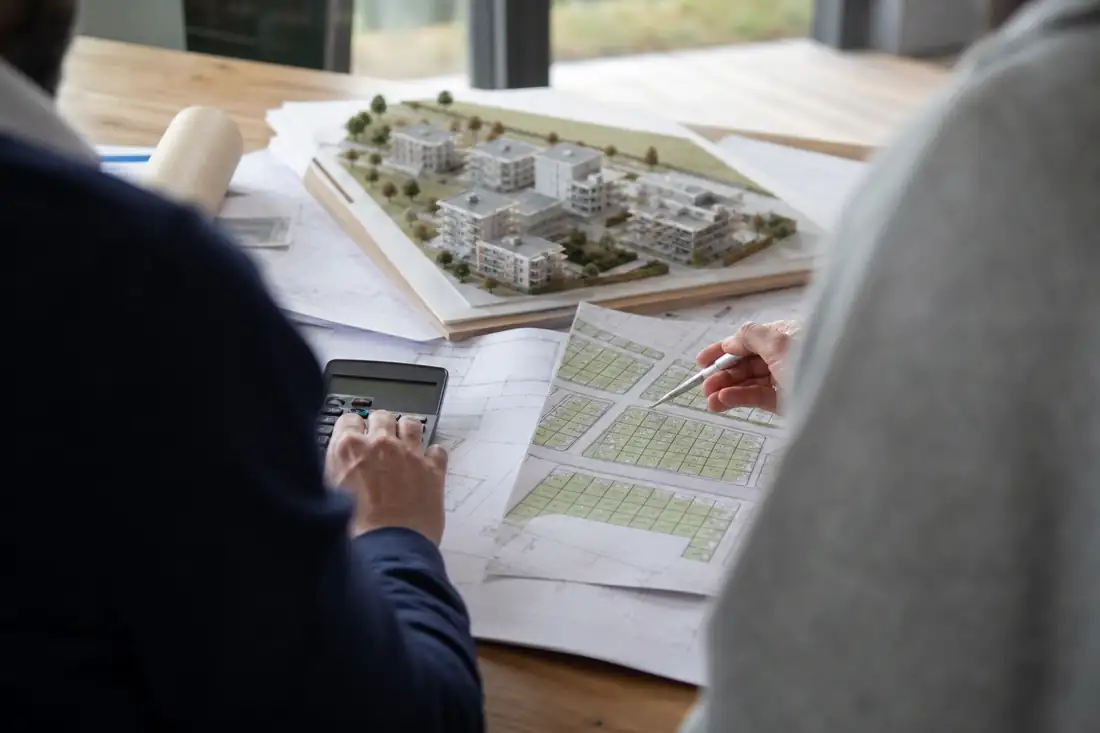 Plans et maquette d’un programme résidentiel examinés lors d’une réunion de faisabilité immobilière.