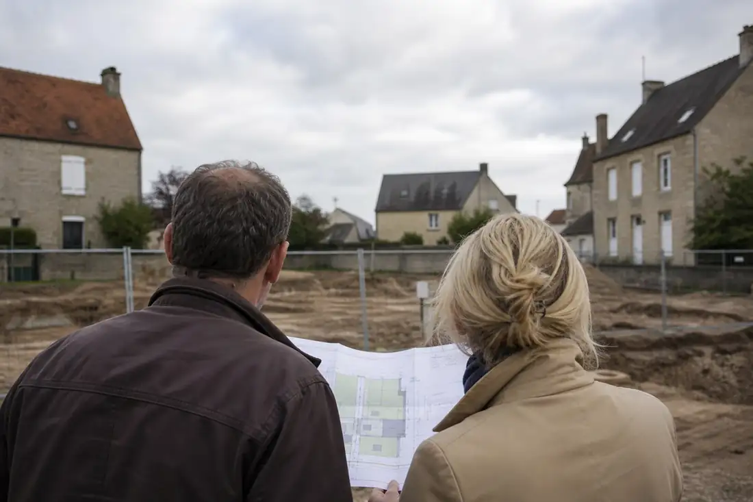 Résidents observant un chantier résidentiel près de maisons en pierre dans une commune rurale de l’Orne.