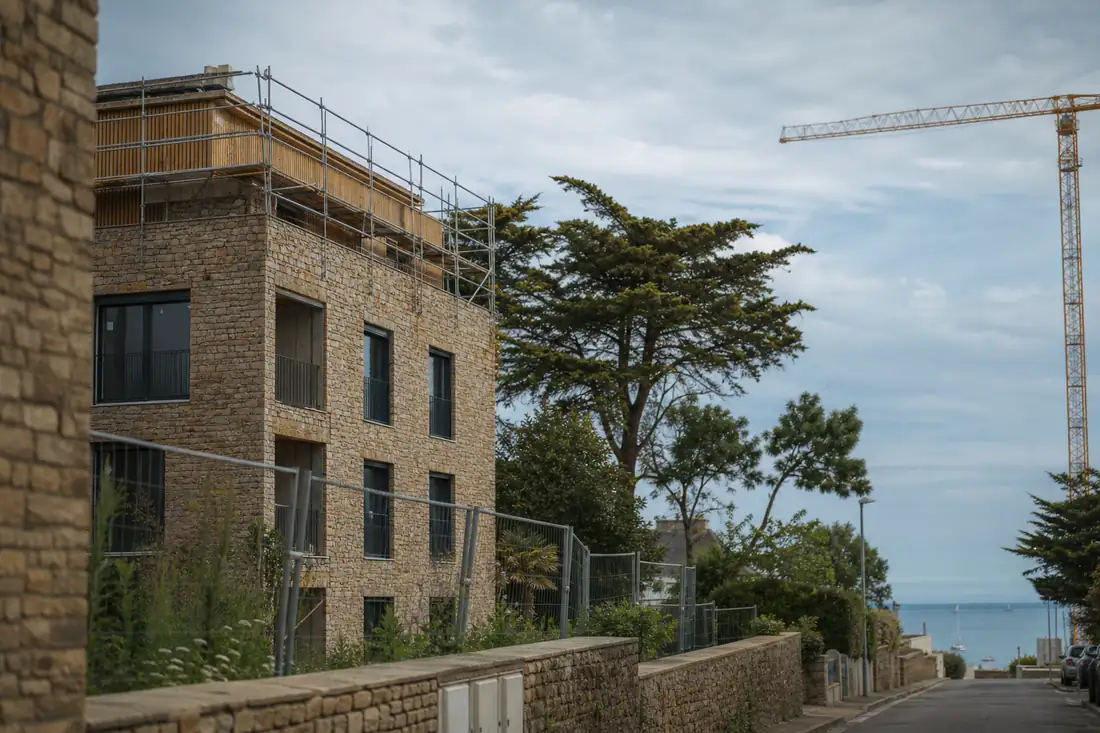 Immeubles contemporains en construction près du littoral malouin, avec grue et façades en pierre.