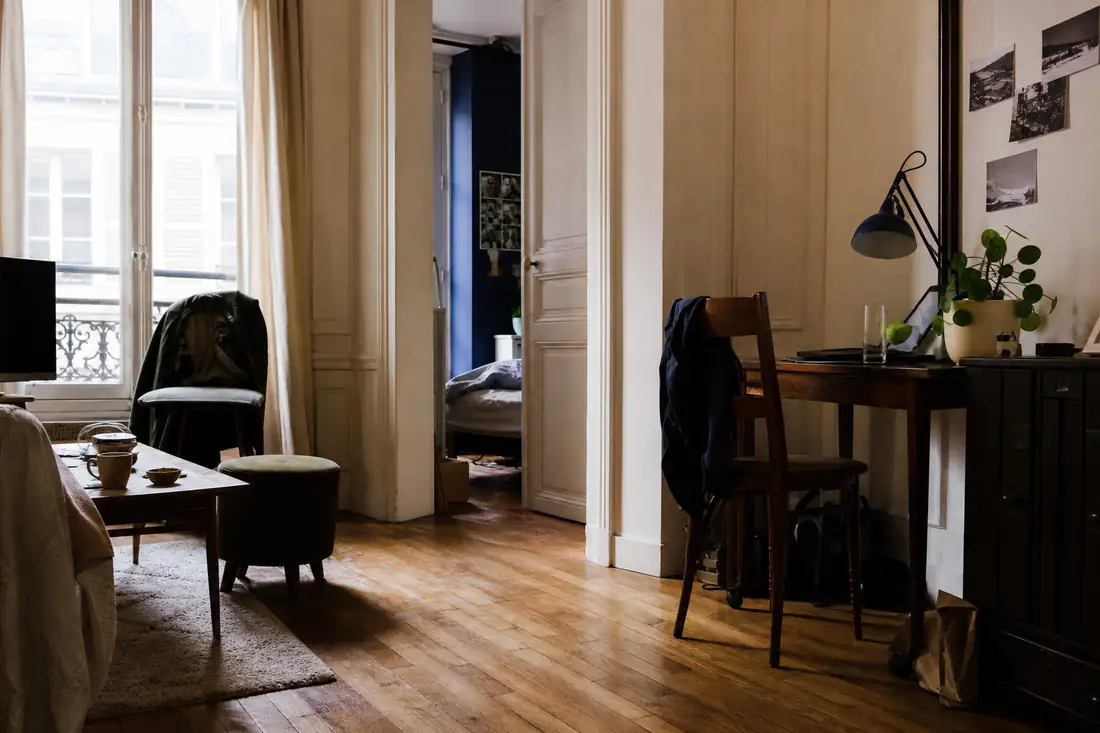 Séjour meublé d’un appartement ancien occupé, parquet et grande fenêtre laissant entrer la lumière du jour