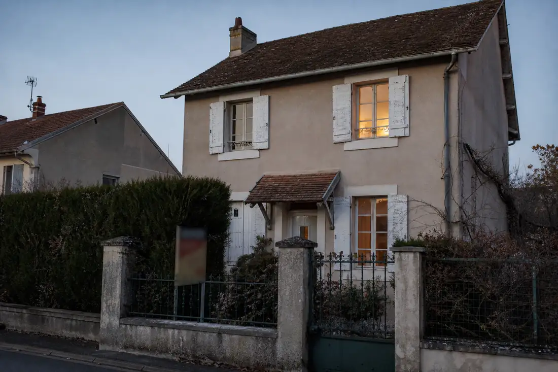 Maison individuelle avec un panneau de vente près du portail, en fin de journée