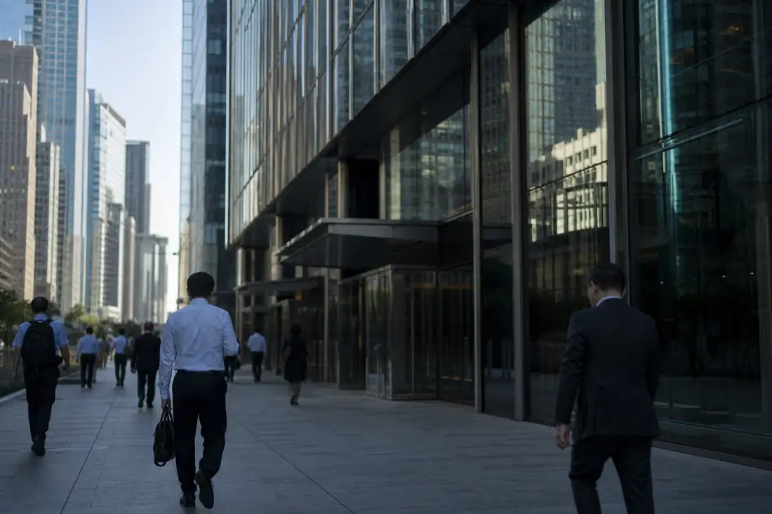 Tour de bureaux moderne vue depuis une place urbaine, avec passants anonymes au premier plan.